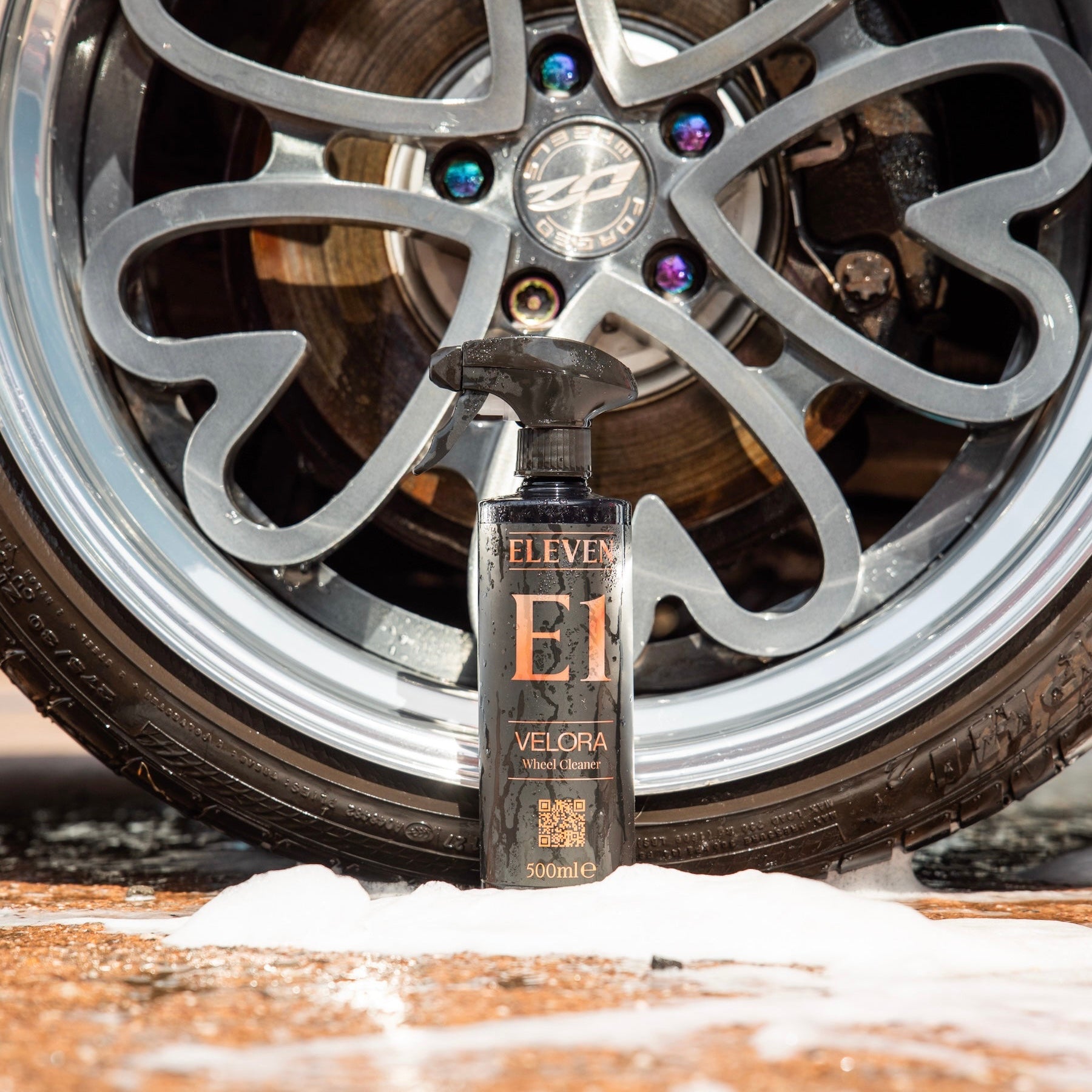 Bottle of Eleven Velocra wheel cleaner in front of a car wheel