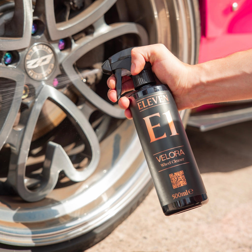 Hand holding a bottle labeled 'Eleven Velora' near a car wheel.