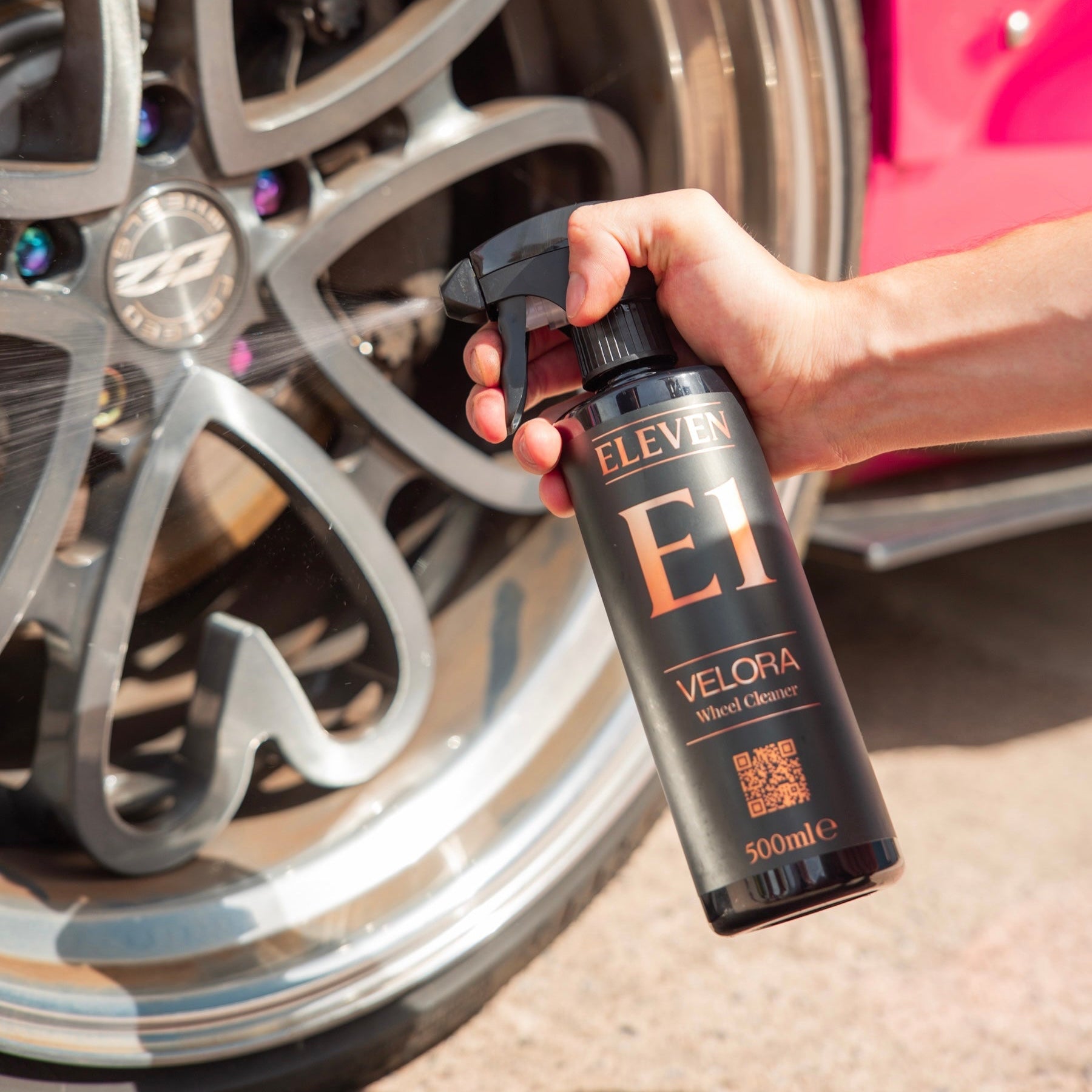Hand holding a bottle labeled 'Eleven Velora' near a car wheel.