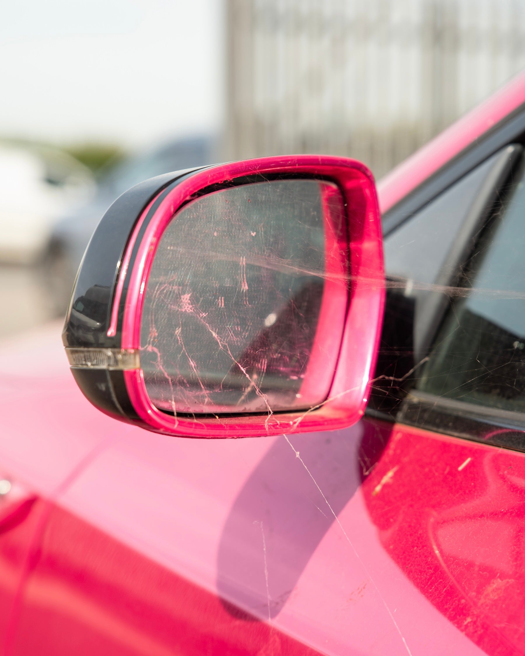 dirty car side mirror on a pink car with blurred background