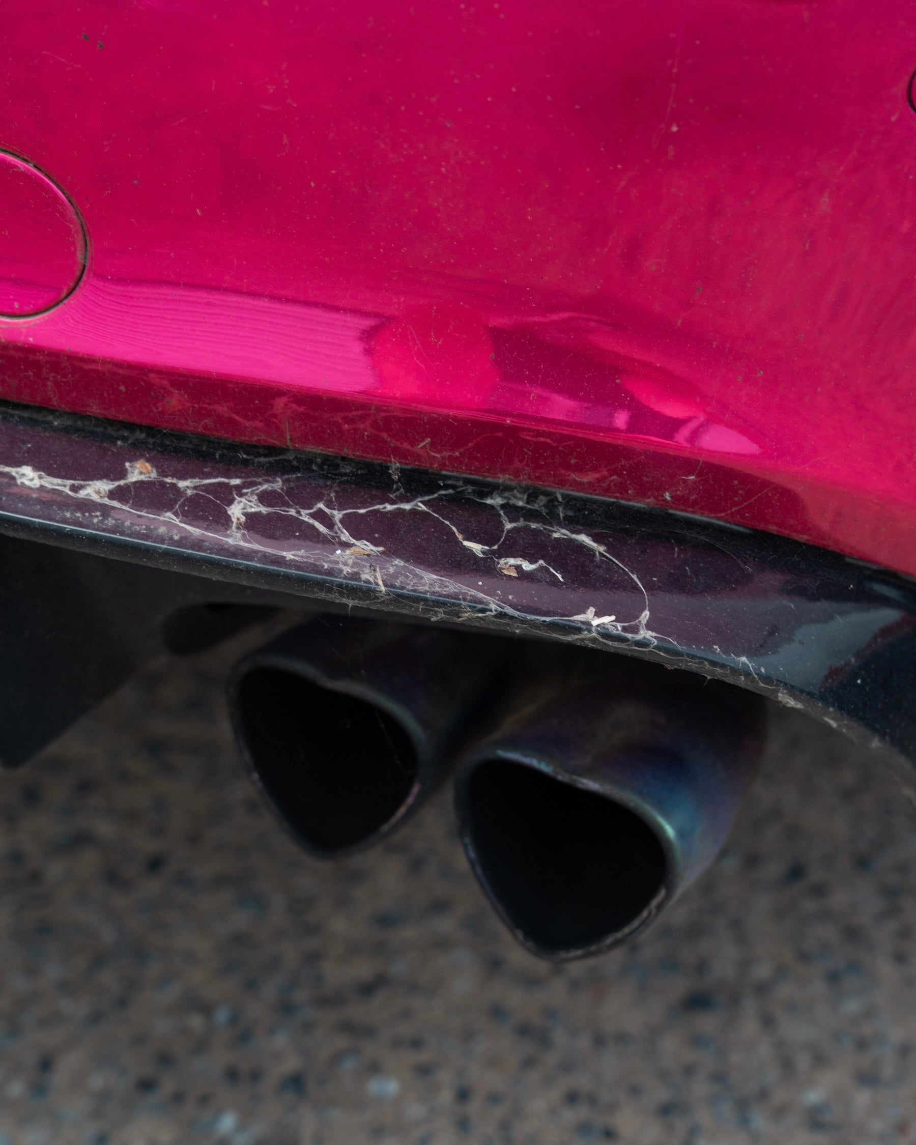 Close-up of a car's exhaust system with a pink car body in the background.
