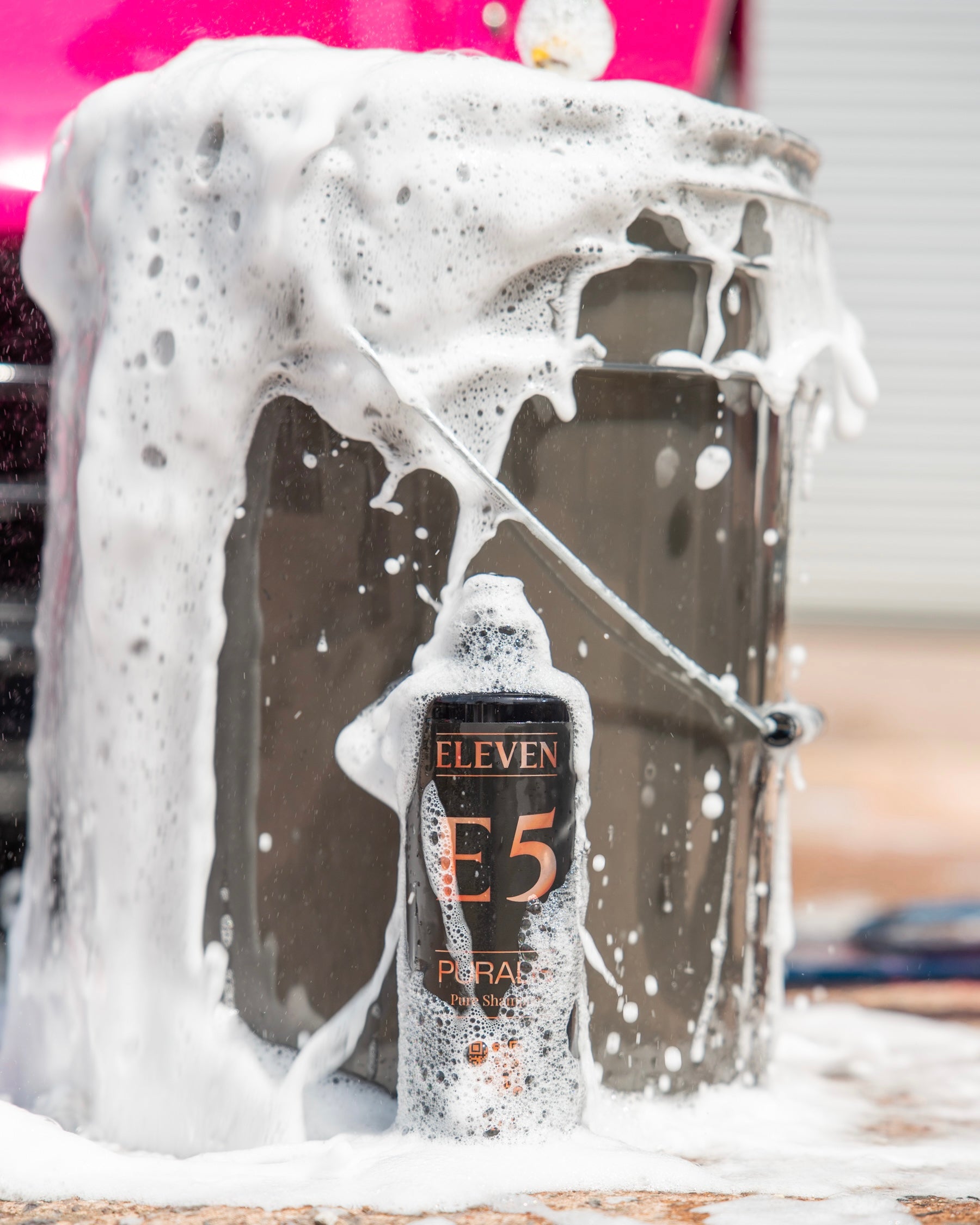 ELEVEN E5 Puralis bottle covered in thick foam in front of a wash bucket  with a pink  car in the background