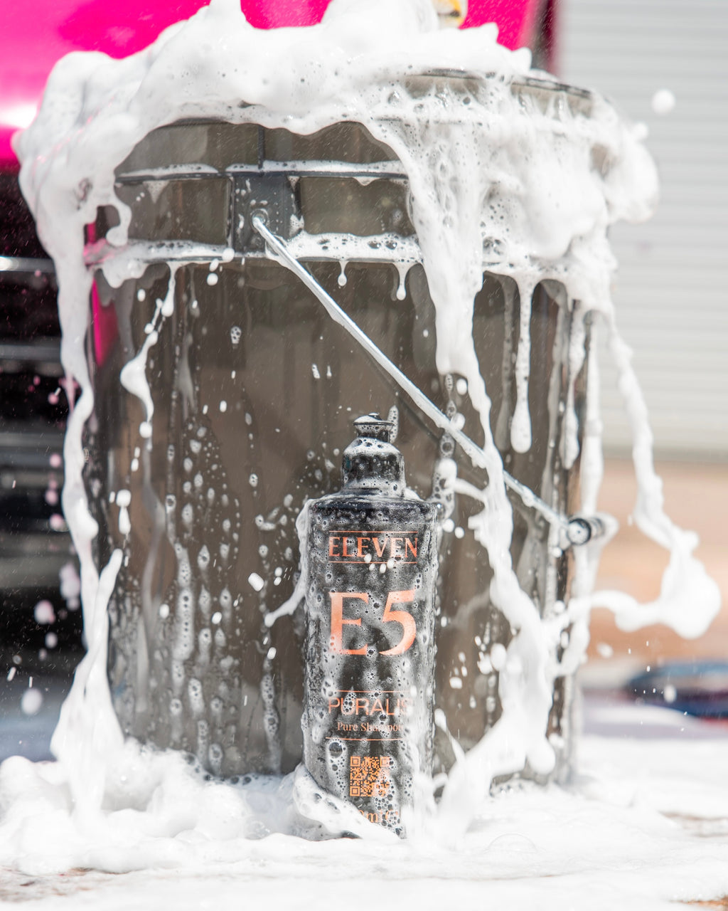 ELEVEN E5 bottle covered in thick foam in front of a bucket with a pink background