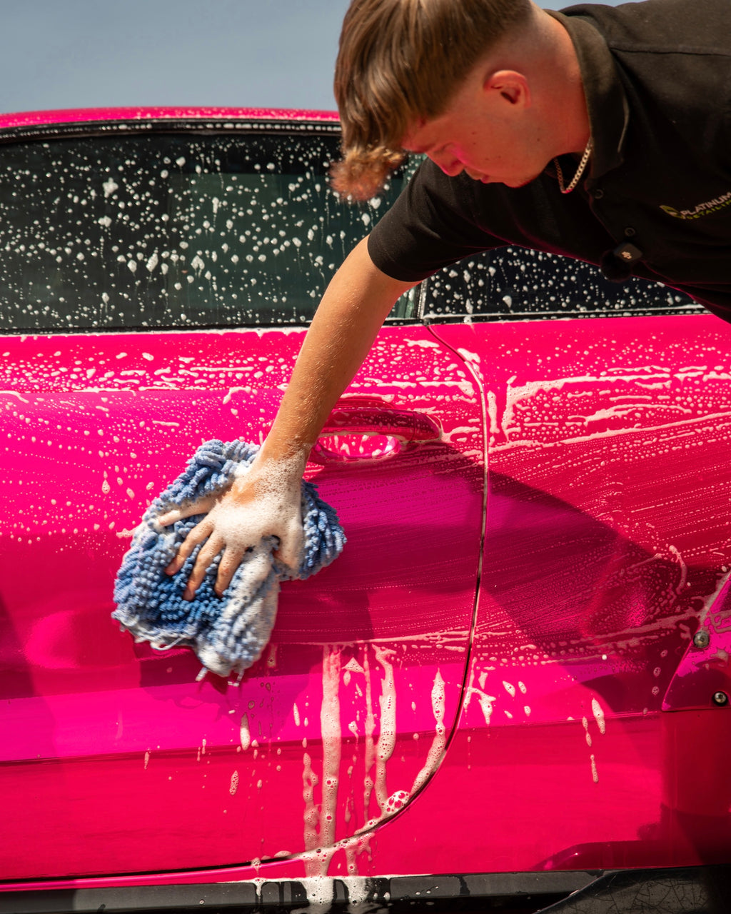 Person washing a pink car with a blue sponge inside a detailing workshop