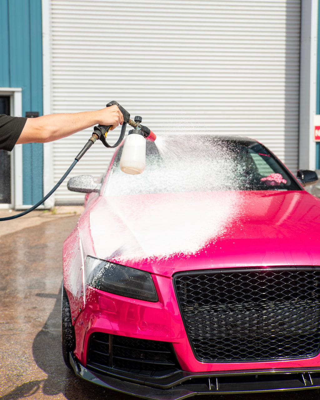 Person washing a pink car with a foamer